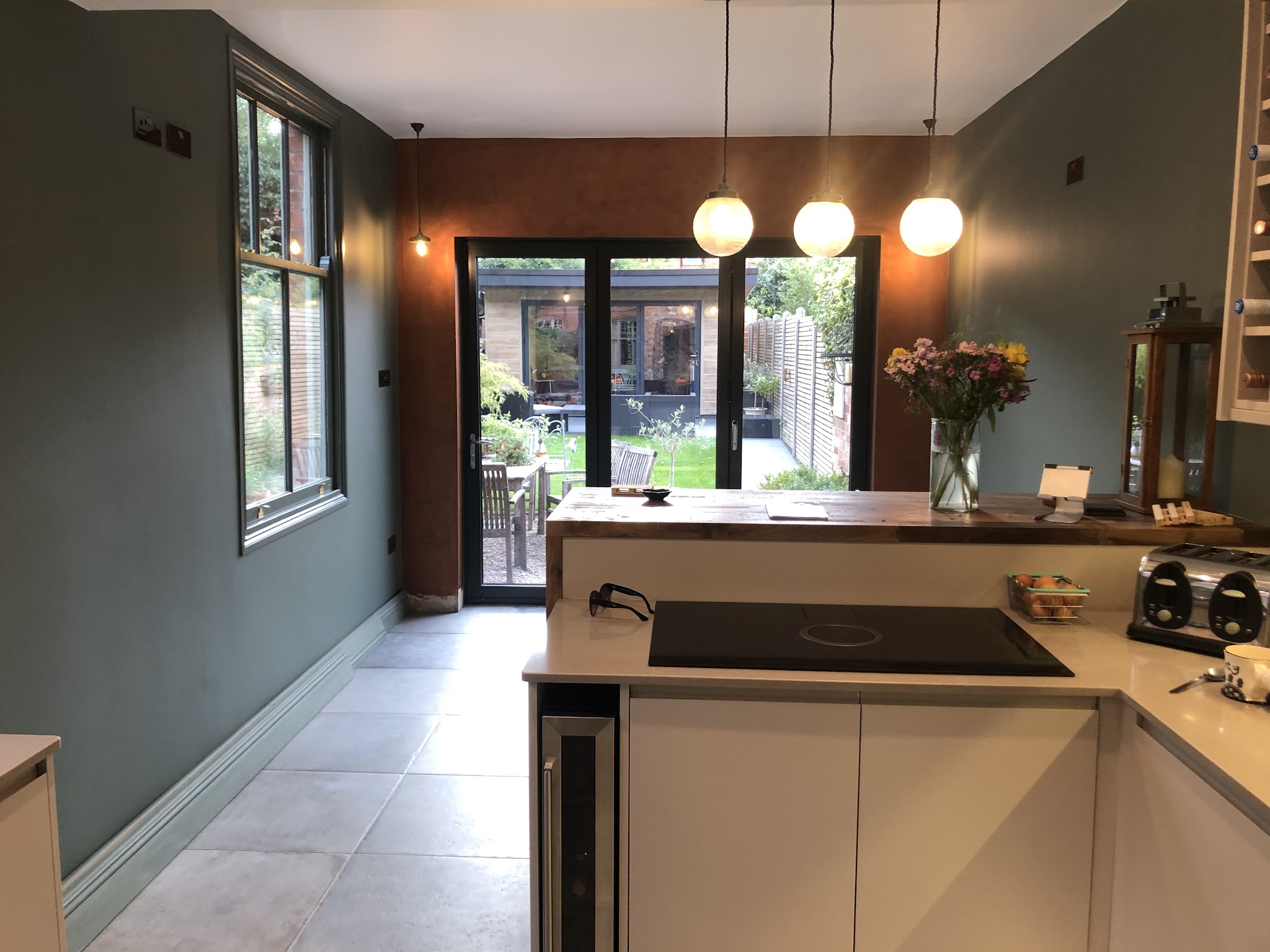 Finished kitchen with deep green walls, a copper feature wall and pendant lights