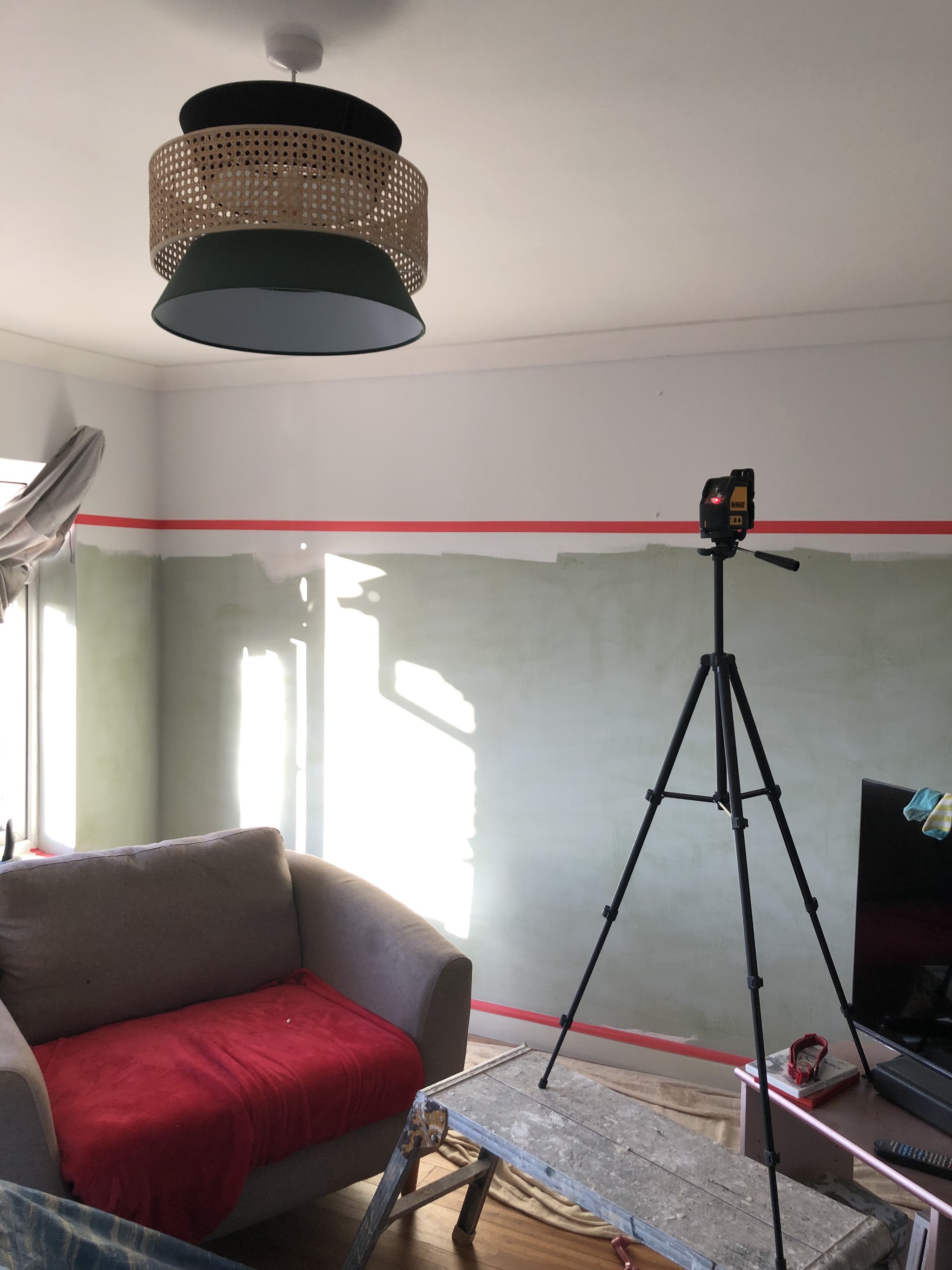 Laser level on a tripod throwing a red line across a living room wall, furniture covered