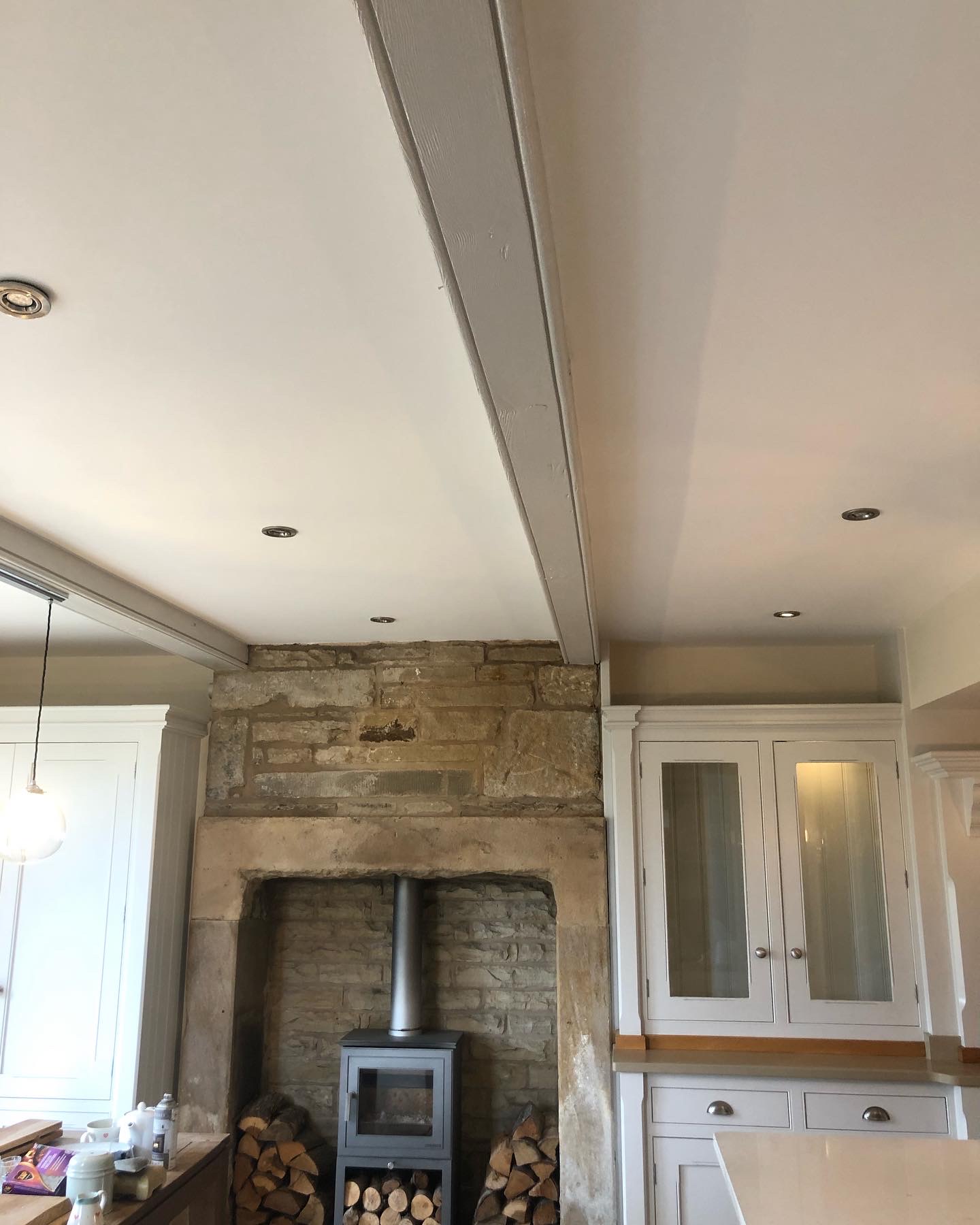 Cream room with an exposed stone fireplace, log burner and painted cabinets