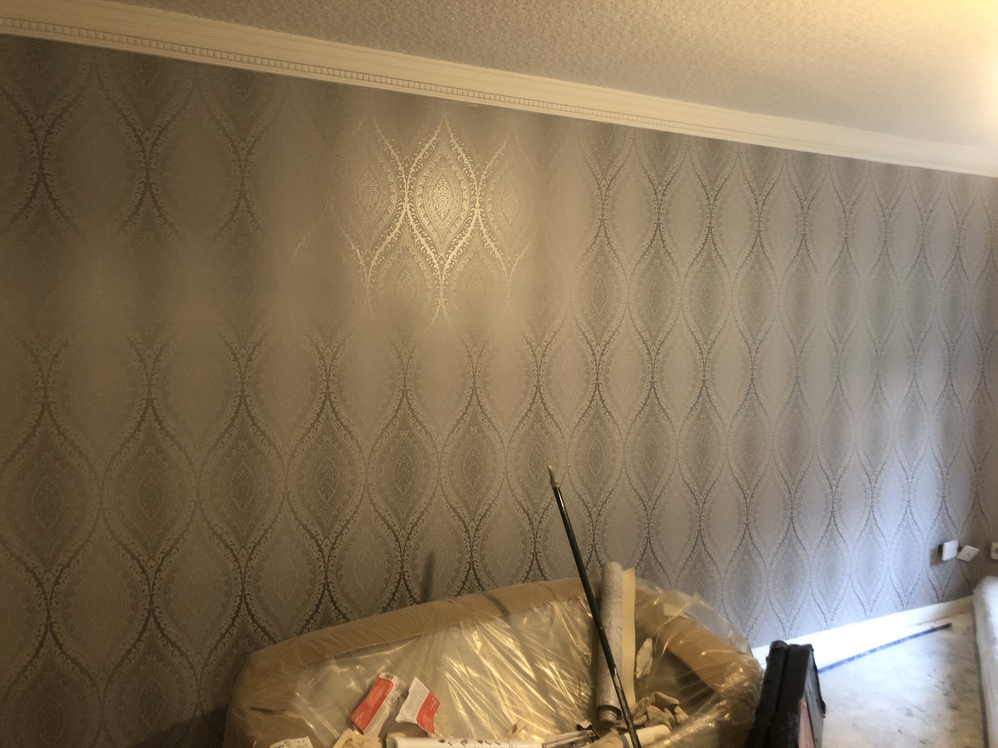 Silver and grey patterned feature wallpaper freshly hung on a living room wall